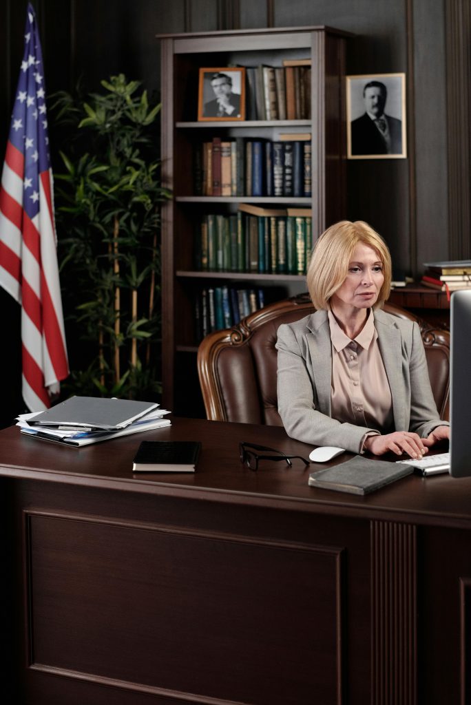 pexels photo 4427426 4427426 A businesswoman in a formal office with an American flag background, working at her desk.