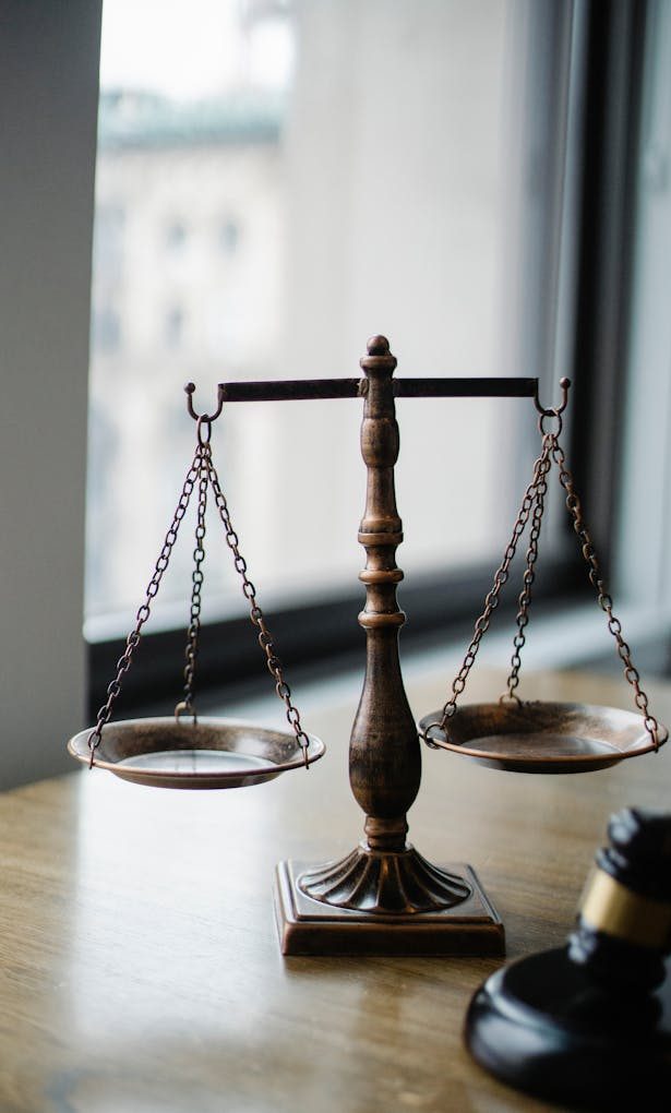 Decorative judgement scale and gavel placed on desk in light lawyer office against window